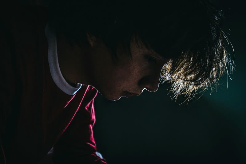 Athlete in a dark hall with head bowed, rim light catching hair and the edge of the face.
