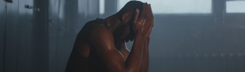 Athlete sitting with head in hands in a dim locker room