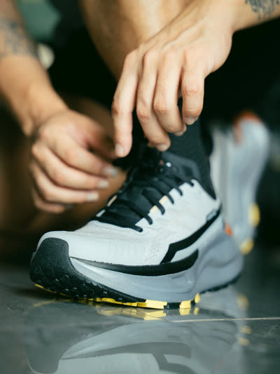 Hands tying the laces of a running shoe on a polished floor.