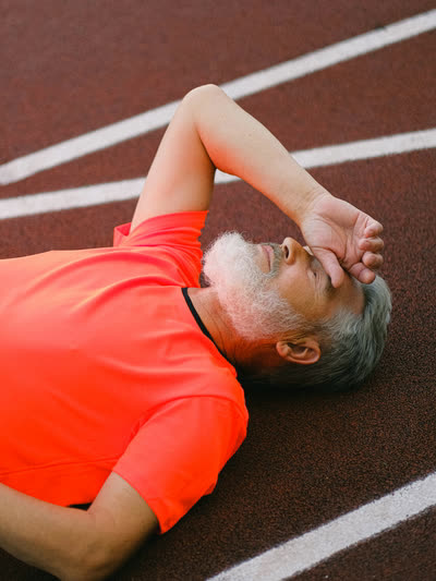 Runner lying on a track with a forearm over his eyes.