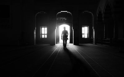 Silhouette of a person walking through a bright doorway into a dark hall