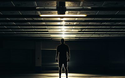 Lone athlete standing in a dark sports hall under a row of ceiling lights