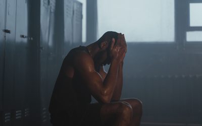 Athlete sitting with head in hands in a dim locker room