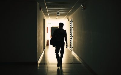 Man with a bag walking away down a dark corridor toward the light