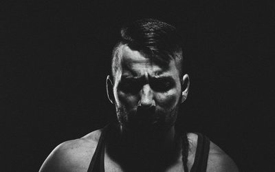 Bearded athlete in a black tank top lit from one side against black